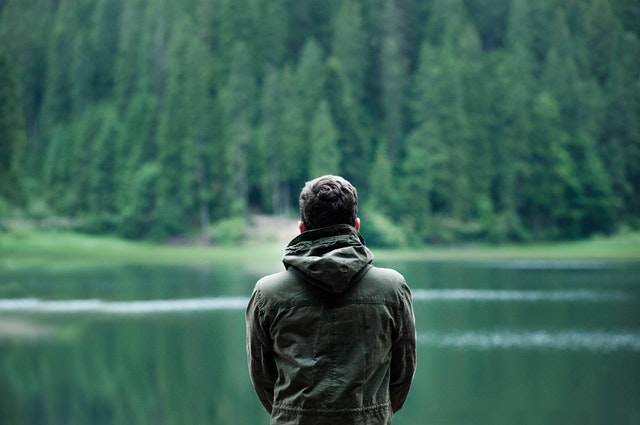 muž stojí v bundě před jezerem